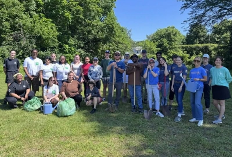 Group of volunteers posing with lawn care equipment in a field