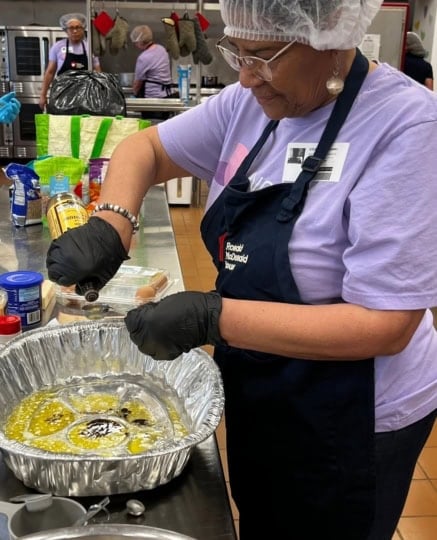 Woman wearing purple shirt and apron pouring oil into pan