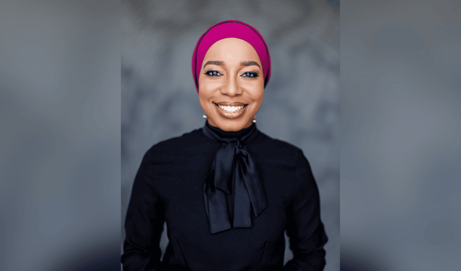 Woman wearing pink hijab and dark blue scarf and top smiling at camera