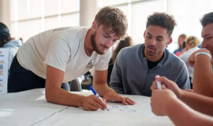 Two college students drawing on sheet spread on table in a large room