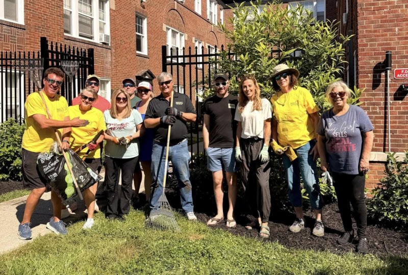 Group of people standing outside apartments with gardening tools smiling at camera
