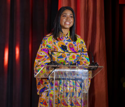 Woman with shoulder length dark hair wearing multi-colored dress smiling at podium