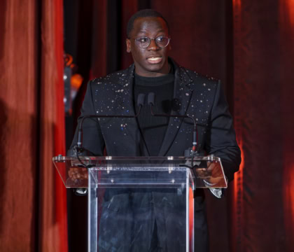 Man wearing glasses and dark suit speaking at podium