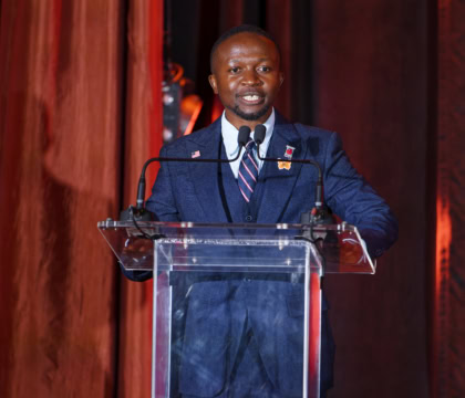 Man in navy blue suit wearing striped tie speaking at podium