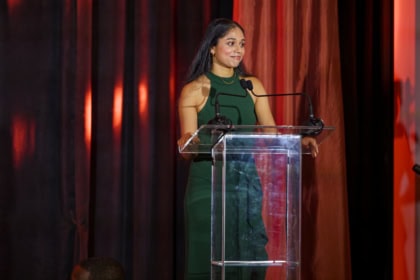 Woman with dark hair wearing emerald dress speaking at podium