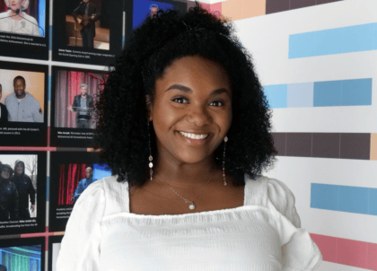 Woman with curly hair wearing white top smiling at camera
