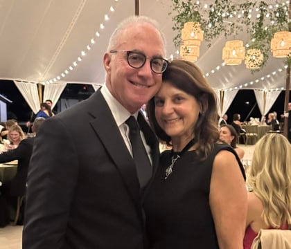 Man and woman in dark formal wear at an event smiling at camera