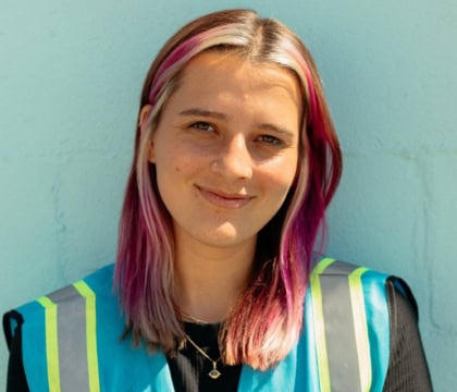 Woman with pink hair wearing blue safety vest looking at camera