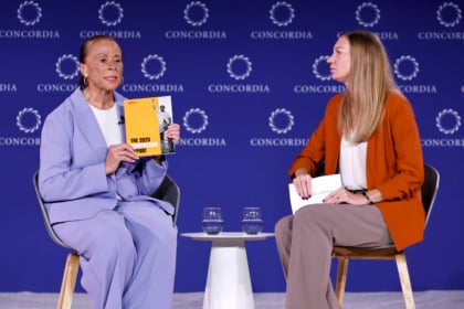 Lonnie Ali wearing purple suit sitting with woman wearing orange jacket and brown pants during panel discussion