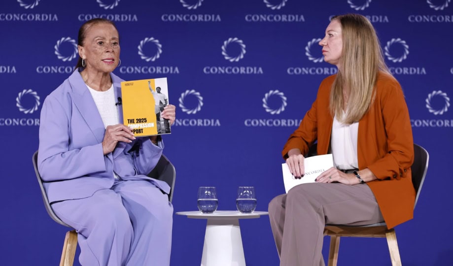 Lonnie Ali wearing purple suit sitting with woman wearing orange jacket and brown pants during panel discussion