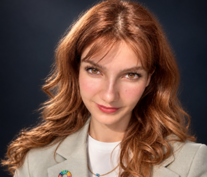 Woman with red hair wearing grey jacket looking directly at camera.